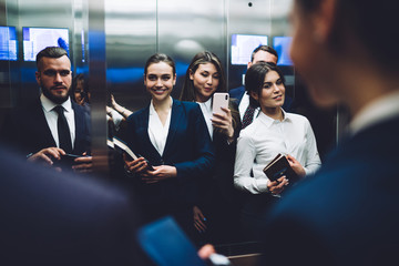 Content coworkers taking selfie while standing in elevator together