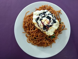Tasty Fried noodle with sunny side up egg. Served on white plate. Top view close up detail