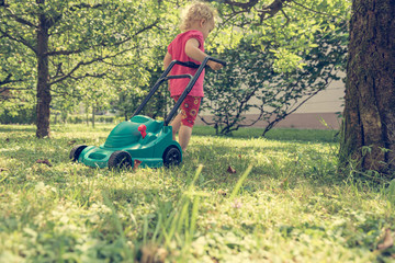 Cute girl lawn mowing with plastic toy mower. - obrazy, fototapety, plakaty