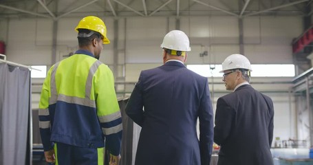 Follow footage of businessmen and workman engineer in hard hat walking through logistics center warehouse or factory. Businessman executive visit - Powered by Adobe