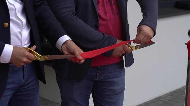 Close up Ribbon cutting at the Grand opening. Closeup of a man's hand cutting a red ribbon with golden scissors