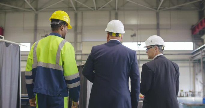 Follow footage of businessmen and workman engineer in hard hat walking through logistics center warehouse or factory. Businessman executive visit