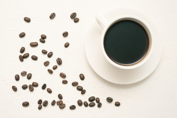 Hot cup of coffee and coffee beans on white table flat lay background.