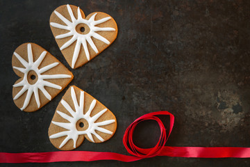 Three gingerbread heart shaped cookies with white icing and red ribbon on dark background 