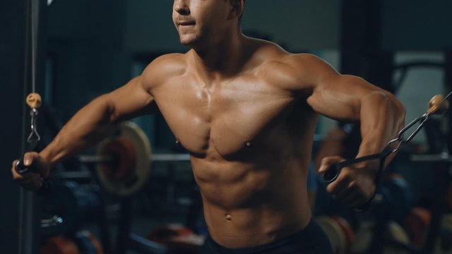 Muscular bodybuilder at cable crossovers fitness men pumping up muscles. Workout fitness exercises and bodybuilding concept background - Handsome athletic men doing bars exercises in gym naked torso