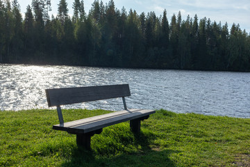 Wooden bench with great view on finish river and pine trees forest with beautiful sky landscape. Recreation area on river. Nobody.