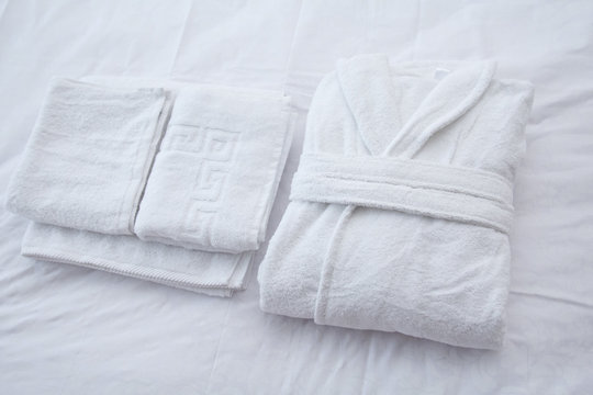Clean folded bathrobe and towels on white bed.