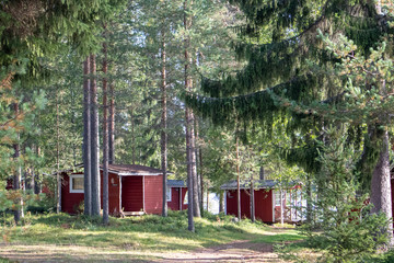 Red wooden finnish traditional cabins cottages in green pine forest near river. Rural architecture...