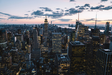 Aerial view of skyscrapers and towers in midtown skyline of Manhattan with evening sunset sky. Scenery cityscape of financial district with famous New York Landmark, illuminated Empire State Building