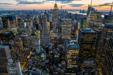 Fotobehang New York Aerial view of skyscrapers and towers in midtown skyline of Manhattan with evening sunset sky. Scenery cityscape of financial district with famous New York Landmark, illuminated Empire State Building  © BullRun