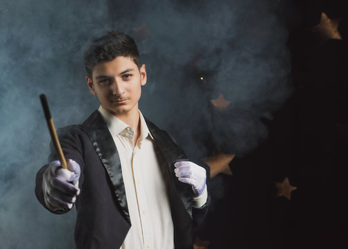  97 / 10000 АНГЛИЙСКИЙ Перевести вGoogleBing Magician with a magic wand on a dark background, charismatic young man in the image of an illusionist