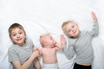 Two older brothers are lying with the youngest baby in a white bed. Happy childhood, big family