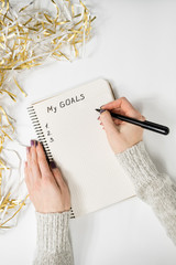 Female hands writing My Goals in a notebook. Tinsel, New Years concept