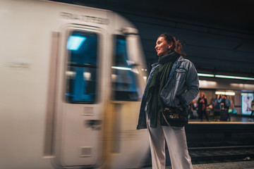 Elegant woman dressed in oversize denim jacket and wide white trousers waiting for a subway train...