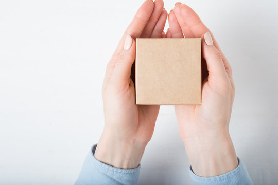 Small Square Cardboard Box In Female Hands. Top View, White Background