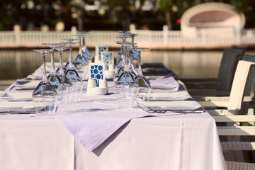 Side view of a served table with a white tablecloth. Served table on the terrace awaiting guests. Cropped shot, horizontal, close-up. Concept of the restaurant industry.