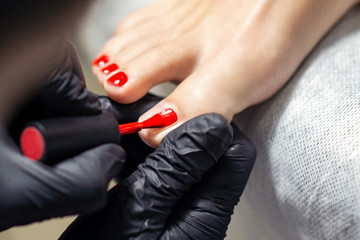 Woman receiving red nail polish on fingers of feet close up.