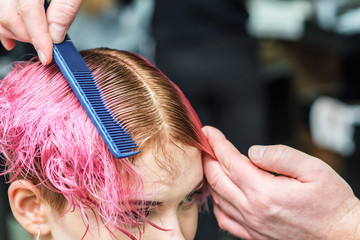 Male hairdresser is combing pink hair of young woman close up in hair salon.