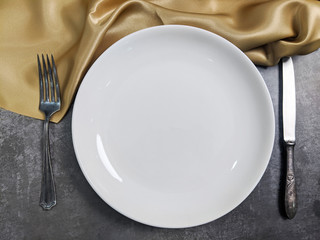 Empty White ceramic plate with fork and spoon on gray stone concrete table background. Copy space. Menu Recipe Concept