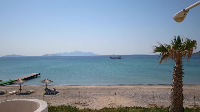 Arriving at the sandy beach on Kos island in Greece. The shot is in motion. Palm trees, wooden pier, sandy beach, beach chairs and umbrellas.