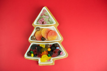 Jelly candies on christmas eve plate on red background. Holidays, sugar dessert concept