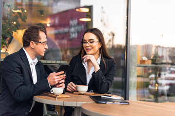 Business people in cafe, working while break. Business-team working on laptop at coffee bar, looking a mobile phone.