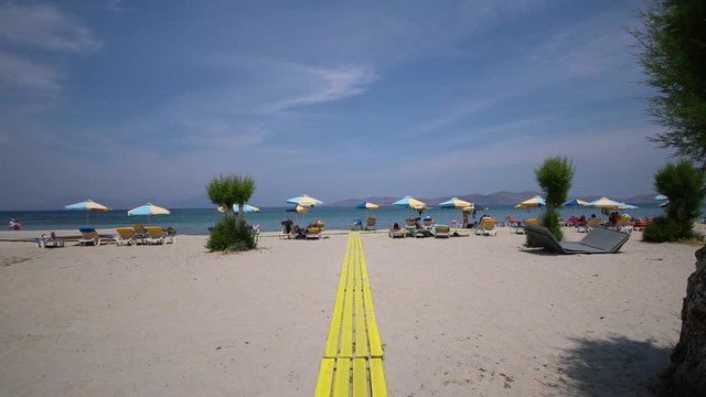 Arriving on a beautiful sandy beach on Kos island in Greece on a wooden walkway. The beach has parasols and beach chairs.