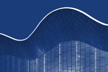 Refined Fragment Of Building On Blue Sky Toned 19-4052. Curvilinear Wavy Architecture Construction in Classic Blue Color. Bottom View Of Modern Architecture Detail. Part Of Building In Abstract Style.