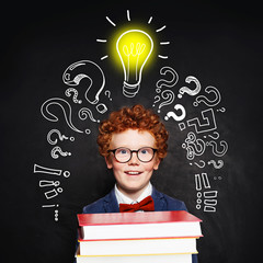 Redhead student child with lightbulb on blackboard background. Idea concept