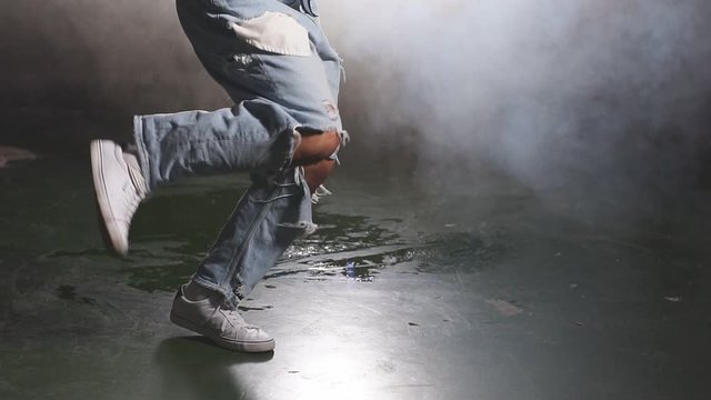 Good-looking stylish man dancing street dance isolated over smoky background, wearing black t-shirt and blue ripped jeans