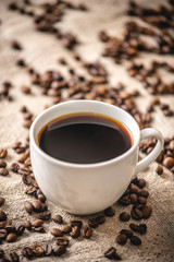 A mug of strong black coffee and scattered grains. Fragrant invigorating drink from freshly roasted coffee beans