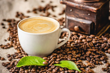 Tasse de café avec de la mousse et un moulin à café vintage en bois. Boisson vivifiante parfumée à base de grains fraîchement torréfiés.