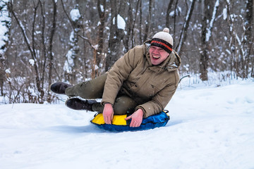 Fototapeta na wymiar Cheerful guy rolls down the hill on snow tubing in the woods . Sledding. Winter entertainment.