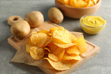 Potato chips. Beer snacks, sauce, potato on cutting board, on grey background, space for text. Closeup