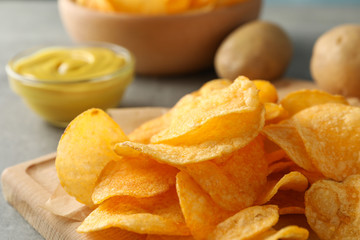Potato chips. Beer snacks, sauce, potato on cutting board, on grey background, space for text. Closeup