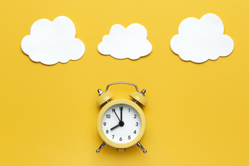 Yellow round alarm clock and white clouds on the yellow background.