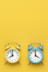 Two round alarm clocks yellow and blue on the yellow background.