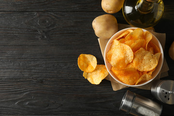 Potato chips in a bowl on craft paper. Potato, spice, olive oil on wooden background, space for text