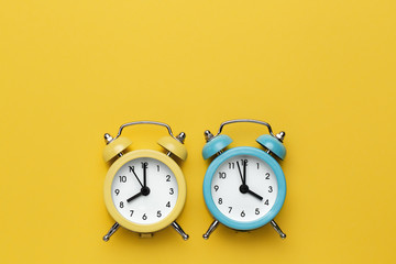 Two round alarm clocks yellow and blue on the yellow background.
