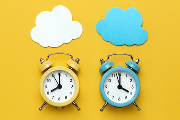 Two round alarm clocks yellow and blue and clouds on the yellow background.