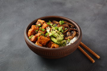 Sweet, spicy , crispy and fried Tofu in teriyaki sauce served in a bowl with avocado,fried mushrooms, sesame seeds and rice. Healthy vegan food, gluten-free