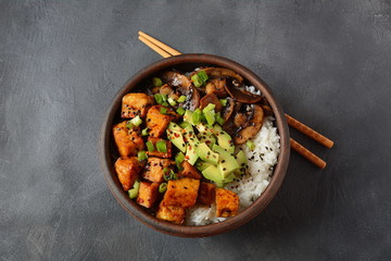 Sweet, spicy , crispy and fried Tofu in teriyaki sauce served in a bowl with avocado,fried mushrooms, sesame seeds and rice. Healthy vegan food, gluten-free