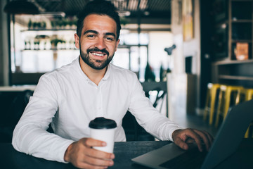 Fototapeta na wymiar Portrait of cheerful caucasian man freelancer sitting in coffee shop with laptop computer working remotely satisfied with income, happy bearded male millennial have successful online business
