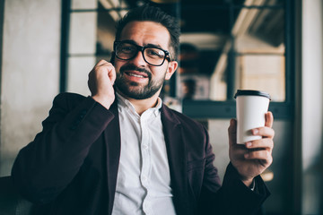 Portrait of cheerful bearded proud ceo talking on smartphone enjoying conversation during coffee break, prosperous businessman in formal wear look in camera making call hold disposable cup .
