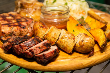 Barbecue meat, grilled sausages and french fries with sauce on a wooden plate. Dish with a lot of fried meat.