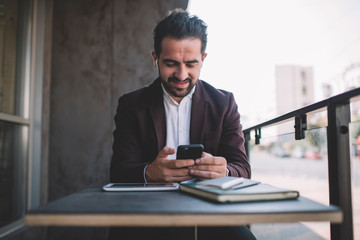  Caucasian man in formal wear on coffee break sending text messages online enjoying radio via wireless bluetooth accessory, smiling successful male manager read news and listen music on cellphone.