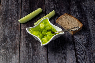 Cucumber jam in a bowl on a wooden background with a slice of bread