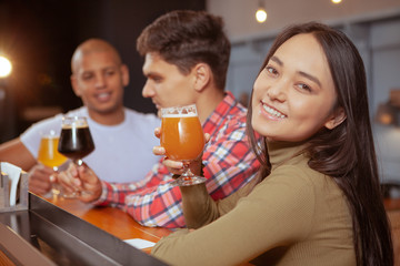 Beautiful happy Asian woman smiling to the camera with a glass of beer, enjoying celebrating with her friends at the pub