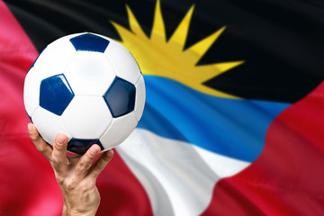 Antigua and Barbuda soccer concept. National team player hand holding soccer ball with country flag background. Copy space for text.