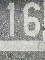 Number 16 written on street asphalt as a parking lot place for a car with leaves and street dirt around in an urban setting
